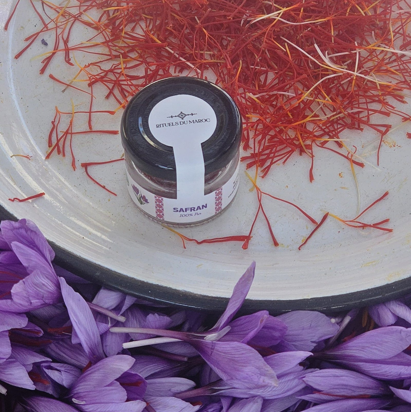 Pot de safran pur Rituels du Maroc entouré de fleurs de safran et pistils récoltés à Taliouine